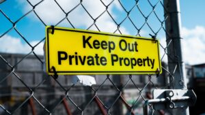 Yellow Keep Out Private Property sign on chain link fence representing property protection and possessory rights. Photo by Unsplash contributor.