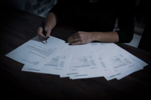 Mulher assinando contrato de imóvel com documentos espalhados sobre a mesa, representando o processo de registro de propriedade. Photo by Unsplash