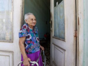 Idosa sorridente com andador na porta de sua residência, representando o público do BPC LOAS