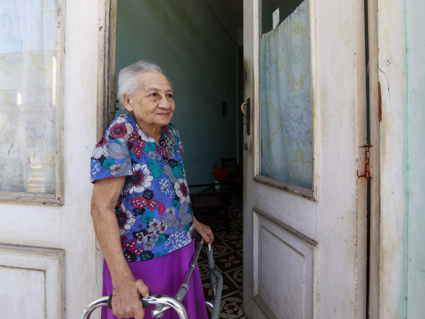 Idosa sorridente com andador na porta de sua residência, representando o público do BPC LOAS