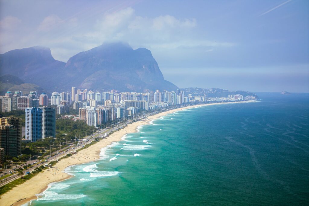 Vista aérea da Barra da Tijuca com praia, prédios de alto padrão e montanhas ao fundo, Rio de Janeiro