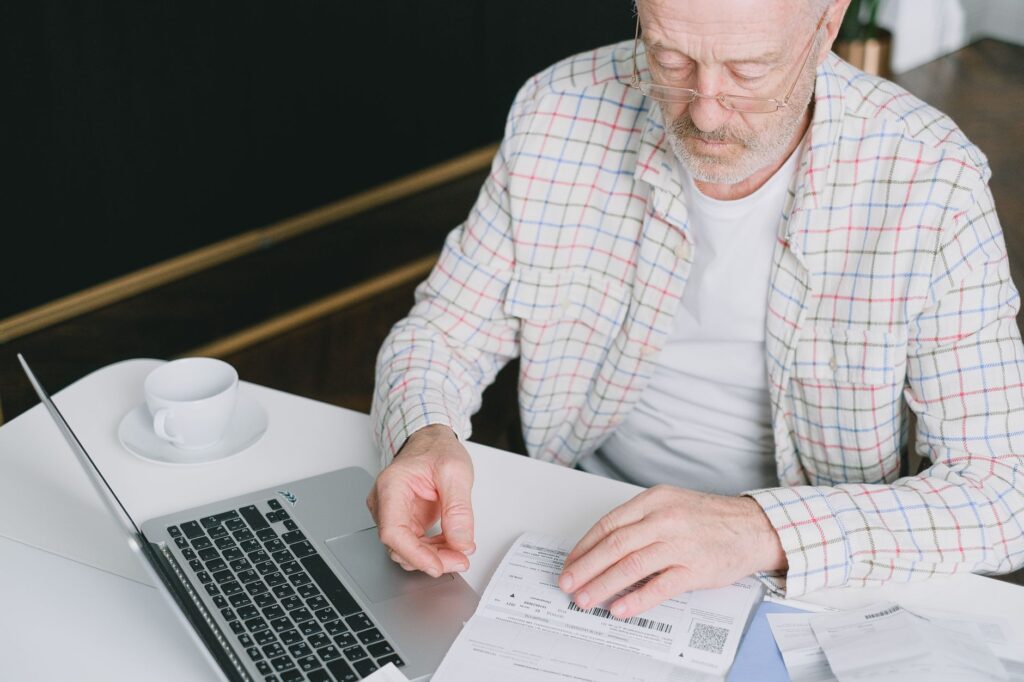 Homem idoso com óculos revisando documentos previdenciários em frente a notebook, representando o Direito Previdenciário