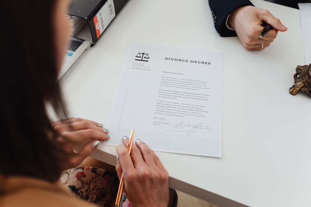 Mulher assina decreto de divórcio em mesa de escritório jurídico com advogado ao lado