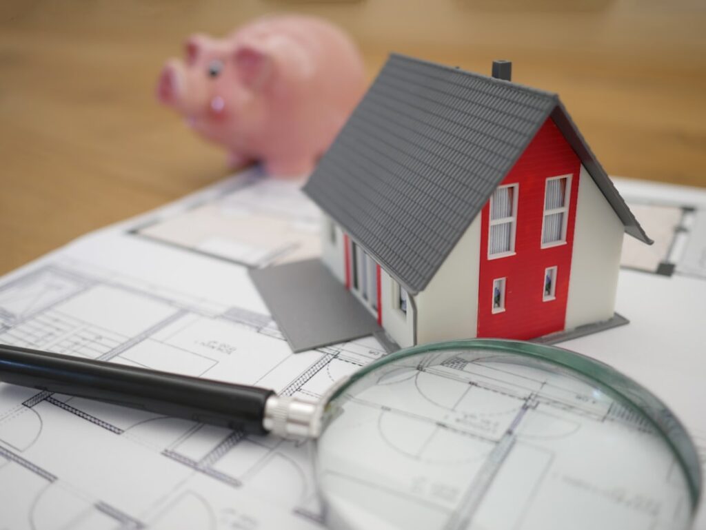 Miniatura de casa sobre planta baixa com lupa, simbolizando o mapeamento patrimonial e avaliação de imóvel no divórcio