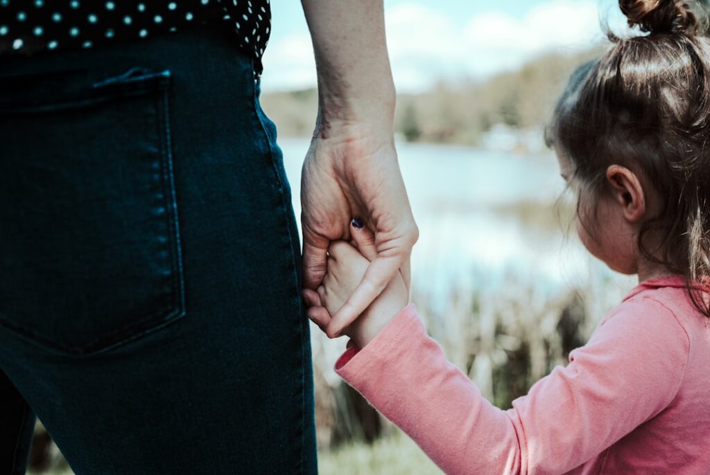 Pai ou mãe segurando a mão de filha pequena, representando guarda compartilhada no divórcio consensual
