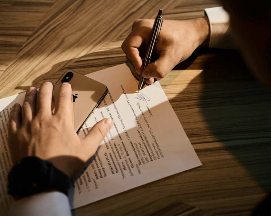 Pessoa assinando documento jurídico de sucessão testamentária com caneta sobre mesa de madeira