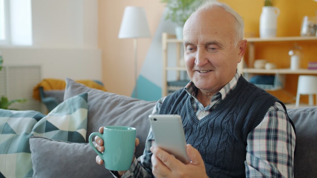 Idoso aposentado usando smartphone em casa para acessar o aplicativo Meu INSS e solicitar atendimento previdenciário online